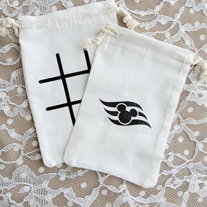 Puede incluir: Dos bolsas de tela blanca con cordón. Una bolsa tiene un tablero de tres en raya negro impreso en ella. La otra bolsa tiene una cabeza de Mickey Mouse negra con un diseño de onda blanco y negro impreso en ella.