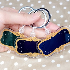 May include: Three gold-colored keychains with a star design. Each keychain has a different colored background: green, blue, and dark blue. The keychains are attached to silver key rings.