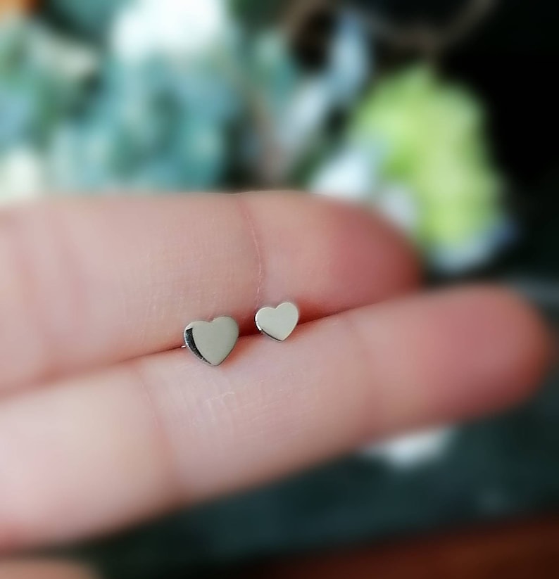 May include: A pair of silver heart-shaped stud earrings. The earrings are small and delicate, and they are perfect for everyday wear.