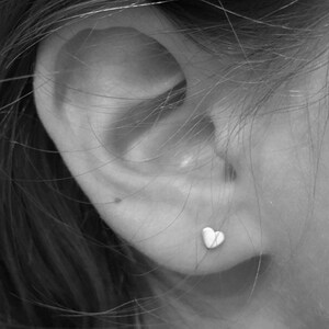 May include: A close-up of a person's ear with a small, silver heart-shaped earring.
