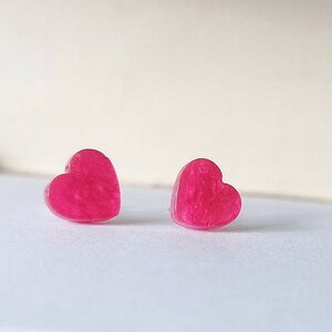 May include: A pair of pink heart-shaped earrings with a glittery finish.