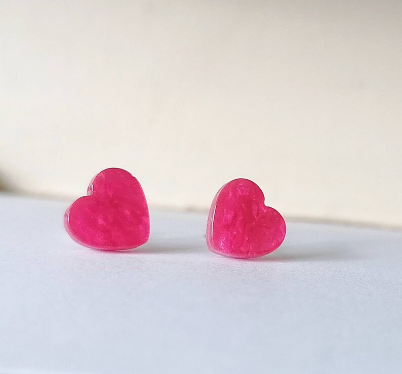 May include: A pair of pink heart-shaped earrings with a glittery finish.