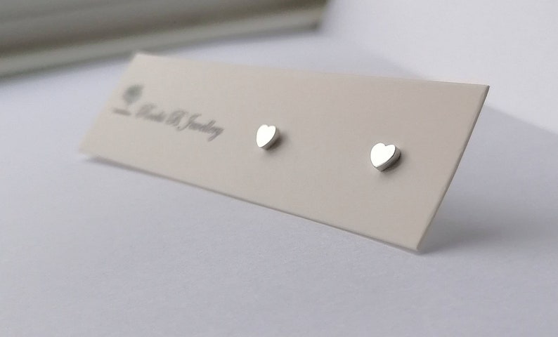 May include: A pair of silver heart-shaped stud earrings on a white card with the text "Roots & B Jewelry".
