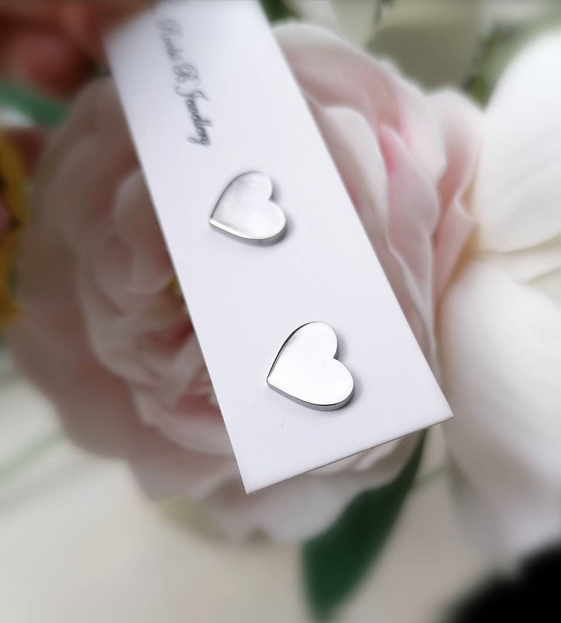 May include: Two silver heart-shaped stud earrings on a white card with the text "Bead & S Jewelry".