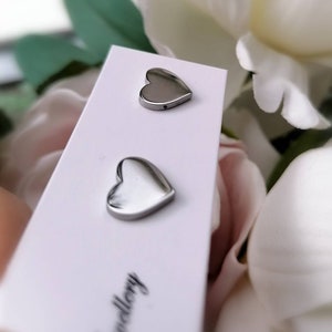 May include: A pair of silver heart-shaped stud earrings on a white card with the word "Jewellery" printed on it.