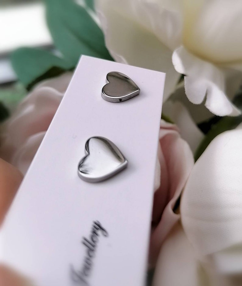 May include: A pair of silver heart-shaped stud earrings on a white card with the word "Jewellery" printed on it.