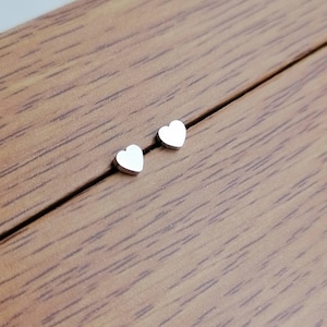 May include: A pair of silver heart-shaped stud earrings on a wooden surface.