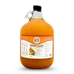 Puede incluir: Una jarra de vidrio grande llena de un l&iacute;quido naranja brillante. La jarra tiene un asa y una etiqueta que dice "Probiotic Elixir, Raw Kombucha Tea, Ginger, Lemon, Turmeric".