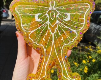 May include: A yellow resin tray shaped like a luna moth with glitter embedded in the resin. The moth has white wings with black outlines.