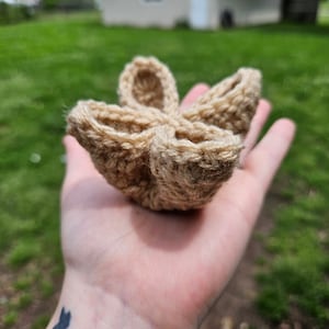 May include: A crocheted flower-shaped bowl made of beige yarn. The bowl is held in a person's hand.