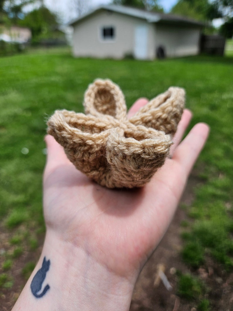 May include: A crocheted flower-shaped bowl made of beige yarn. The bowl is held in a person's hand.