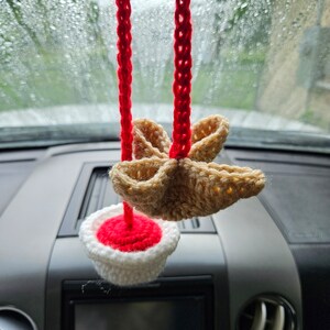 May include: A crocheted car air freshener with a red and white cupcake design and a brown star-shaped top.