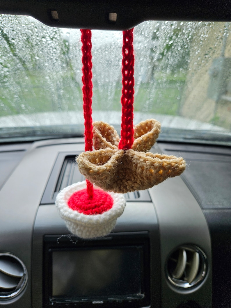 May include: A crocheted car air freshener with a red and white cupcake design and a brown star-shaped top.