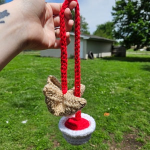 May include: A crocheted toy with a red and white bowl and a brown crocheted bird attached to a red cord.