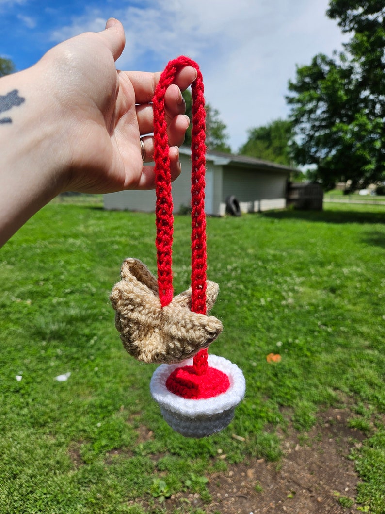 May include: A crocheted toy with a red and white bowl and a brown crocheted bird attached to a red cord.