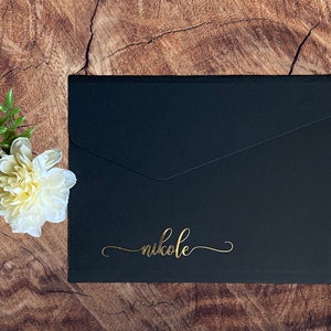 May include: Black envelope with a gold inscription that reads "nikole".