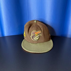 May include: A brown and green baseball cap with an embroidered orange and yellow bird logo. The logo has a black outline and a white beak.