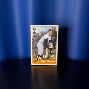 May include: A rectangular book titled Ten Rings: My Championship Seasons by Yogi Berra with Dave Kaplan. The cover features a photograph of a baseball player in a pinstriped uniform kneeling on a field, with a vertical column of ten rings on the left.