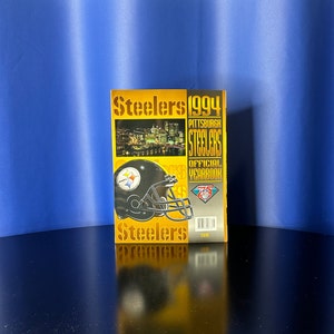 May include: A yellow and black Pittsburgh Steelers 1994 official yearbook with a photo of the city skyline and a football helmet on the cover. The text "Steelers 1994" is in large, bold letters at the top of the cover. The text "Pittsburgh Steelers Official Yearbook" is in smaller letters below the photo. The text "75th Anniversary" is in a small box in the lower right corner of the cover.