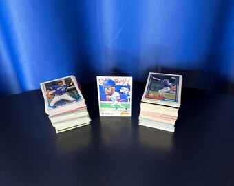 May include: Three stacks of baseball trading cards on a dark surface. The cards feature images of baseball players in action. The background is a solid blue color. The cards are in various colors and designs.