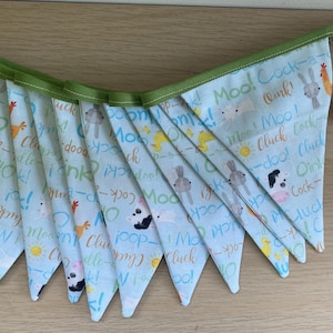 May include: A light blue fabric banner with a green trim, featuring animal illustrations and sound effects like "Moo!" and "Cluck!". The banner includes images of chickens, bunnies, and cows. A small red heart is placed next to the banner.