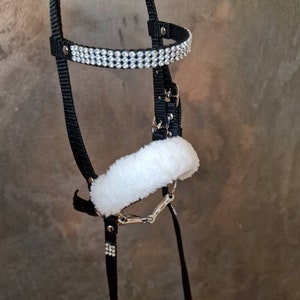Pu&ograve; includere: Un cavezza per cavalli nera con un nasello in pile bianco e una fila di strass argentati.