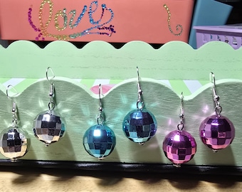 May include: Six spherical disco ball earrings featuring a faceted, mirrored surface. The earrings are arranged in pairs of silver, blue, and purple, each suspended from a silver-toned metal hook. The reflective surfaces create a grid-like pattern.