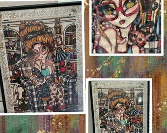 May include: A framed diamond painting of a woman with red glasses and a bun sitting in a chair with cats. The woman is wearing a plaid shirt and pajamas. The painting is set against a background of bookshelves and other home decor.