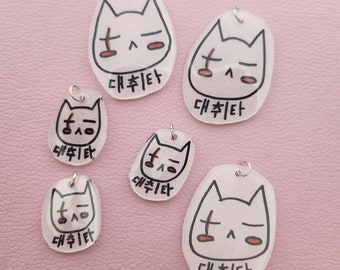 May include: Five white cat-shaped charms with black eyes and a red blush. Each charm has a silver loop for hanging and the Korean text "대취타" written on the bottom.