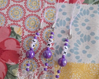 May include: Three beaded phone charms with purple and white beads. Each charm has the letters "JK" and a clear acrylic charm in the shape of a heart or star. The charms are attached to a silver-colored metal loop with a pink string.