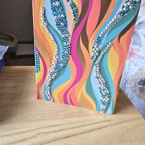 Może przedstawiać: Kolorowy notes z falistym wzorem i niebieskimi i białymi kryształkami.