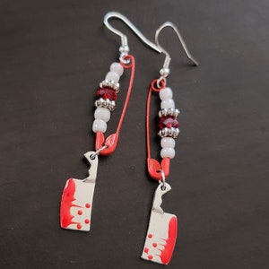 May include: A pair of silver earrings with red and white beads and a red and white painted knife charm.