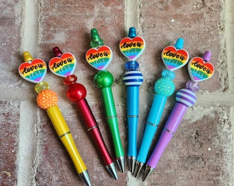 May include: Seven rainbow-colored pens with rainbow heart charms and beads. The charms say "Love is Love".