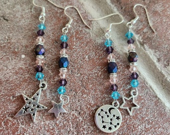 May include: Three pairs of dangle earrings with silver star and constellation charms. The earrings feature pink, blue, and purple beads.
