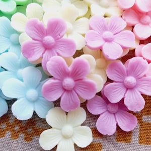 May include: A collection of pastel-colored flower-shaped embellishments. The flowers are in shades of pink, light blue, yellow, and green. Each flower has five petals and a small, round center. These decorative flowers are ideal for crafts.