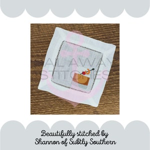 May include: A white linen cocktail napkin with a pink border and a stitched image of a cocktail glass with a cherry and an orange slice. The text "Always Stitches" is embroidered on the napkin.