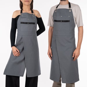 May include: Two grey aprons with adjustable straps and a black pocket. The aprons have a crossover design and are made of a durable fabric.