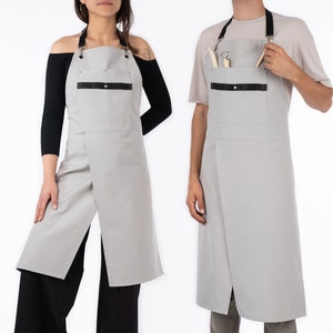 May include: Two grey aprons with black straps and a black pocket. The aprons have a crossover design and are made of a durable fabric.