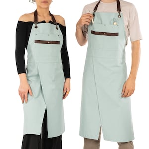 May include: Two light blue aprons with brown leather straps and pockets. The aprons have a crossover design and are made of a durable fabric.