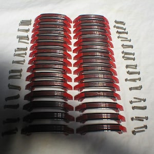 May include: A collection of red and black curved metal pieces with silver screws. The pieces are stacked in rows, with the red accents visible on the edges. The screws are arranged in vertical lines.