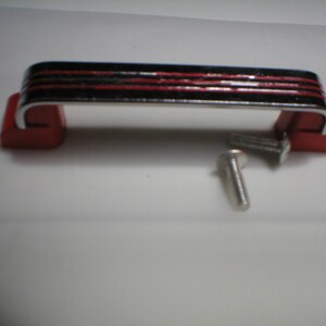 May include: A chrome-plated cabinet handle with red accents and black stripes. The handle is attached to two red plastic bases. Two screws are included.