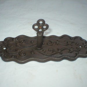May include: A decorative, cast iron key holder with a dark brown finish. The key holder features an ornate, scrolling design on the base and a key-shaped hook. The base is approximately 7 inches long.