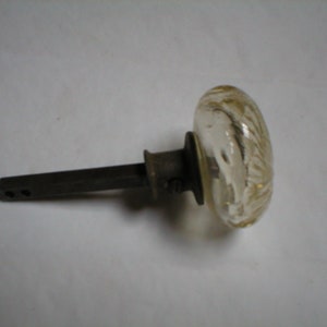 May include: A vintage glass doorknob with a swirling, textured design in shades of gold and clear. The knob is attached to a dark metal stem and mounting hardware, showcasing an antique aesthetic.