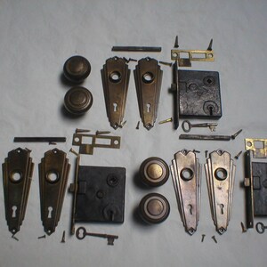 May include: An assortment of antique door hardware, including bronze-toned doorknobs, keyhole covers, and locksets. Various screws, keys, and metal plates are also present, suggesting a complete set for restoration or replacement projects.