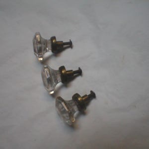Puede incluir: Tres pomos de armario de cristal transparente con forma facetada similar a un diamante. Cada pomo presenta una base met&aacute;lica circular de tono bronce y un tornillo met&aacute;lico corto con rosca en la parte posterior para su instalaci&oacute;n.