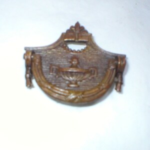 May include: A brown metal decorative door pull with a floral design and a keyhole in the center.