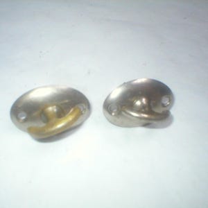 May include: Two metal hooks with a silver-colored base and a gold-colored hook. Each hook has three small holes. The hooks are oval-shaped and appear to be made of metal.