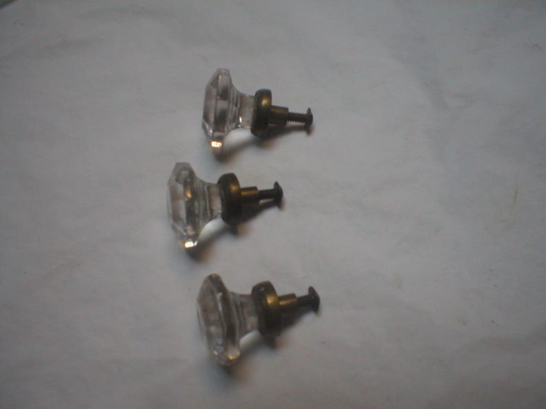 Puede incluir: Tres pomos de cristal transparente para armarios con forma facetada similar a un diamante. Cada pomo presenta una base circular de metal en tono lat&oacute;n y un tornillo met&aacute;lico corto con rosca en la parte posterior para su fijaci&oacute;n.