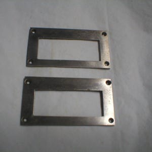 May include: Two rectangular metal plates with a central cutout and four drilled holes in each corner. The plates have a brushed metal finish and are positioned on a neutral background.