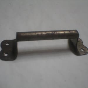 May include: A vintage metal handle with a slightly aged appearance. The handle has a cylindrical grip and two mounting plates with rounded edges and screw holes. The metal has a tarnished, bronze-like color.